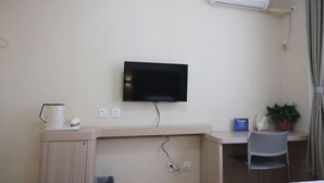A hotel room with a flat-screen TV mounted on the wall, a desk with a chair, a small table with a kettle and a container, and an air conditioning unit. - Xicui Hotel (Beijing Baizhifang) (Beijing)