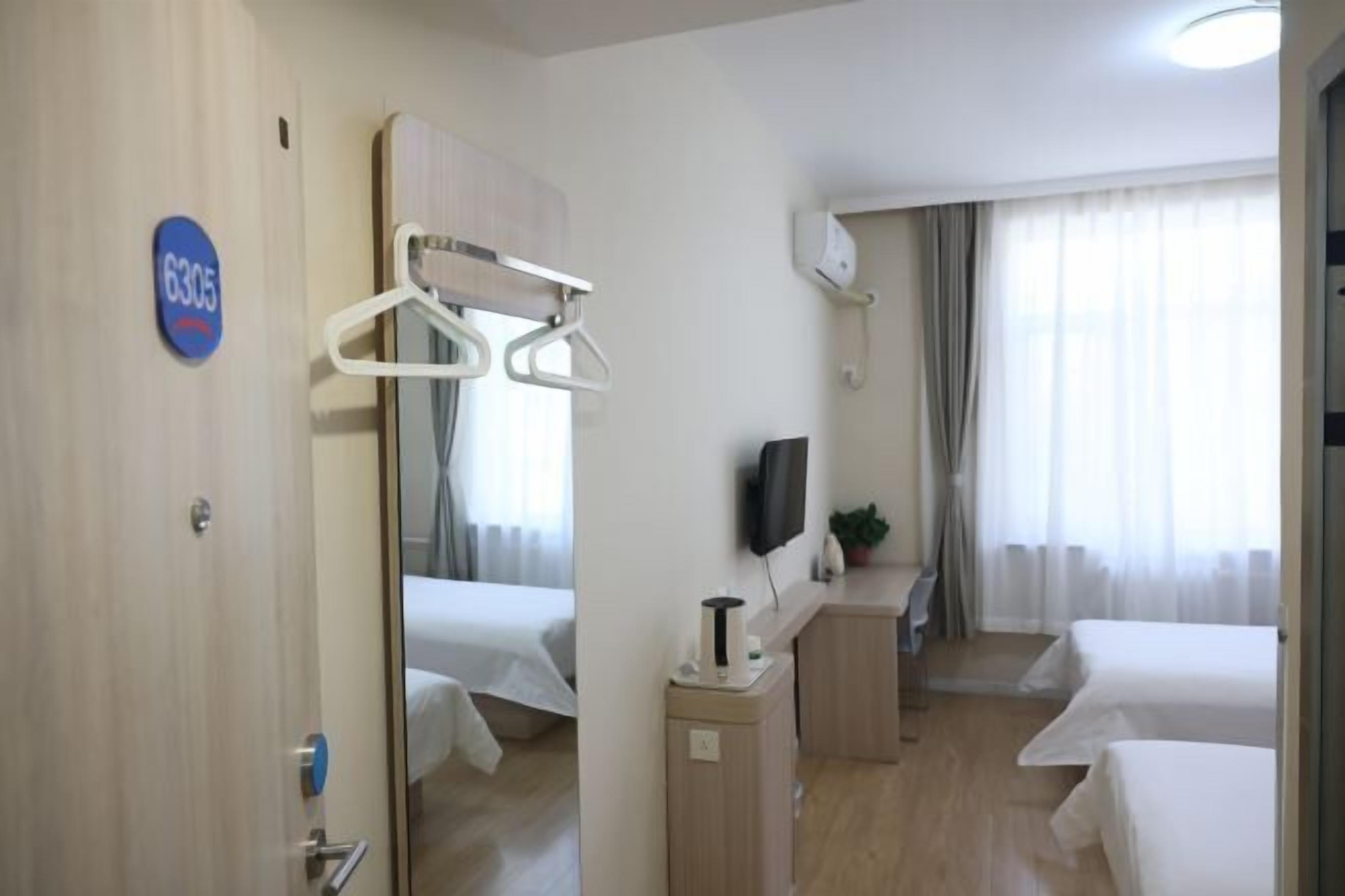 A hotel room with a bed, a desk with a chair, a TV, and a mirror.