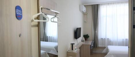 A hotel room with a bed, a desk with a chair, a TV, and a mirror.