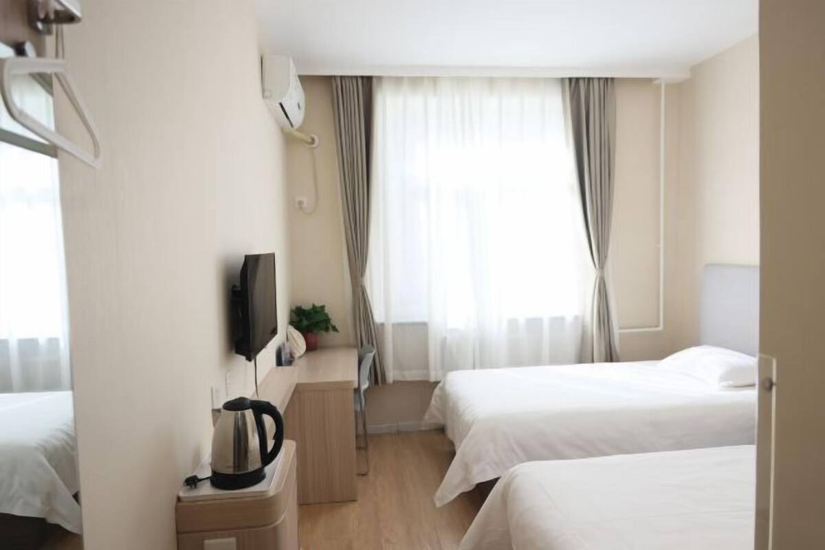 A hotel room with two beds, a TV, a kettle, and a small desk.