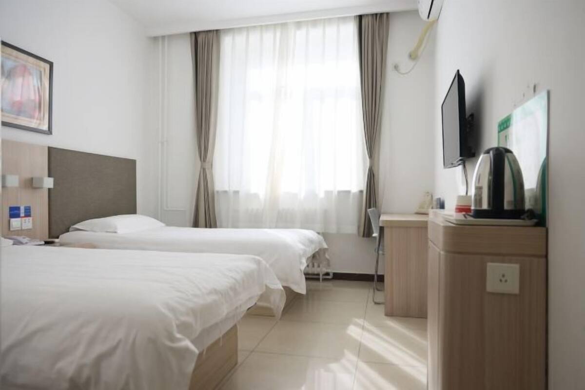 A hotel room with two beds, a desk, a chair, a TV, and a window with curtains.
