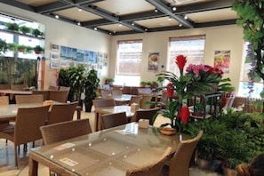 Un restaurante con mesas, sillas y plantas en macetas, además de espacio interior.