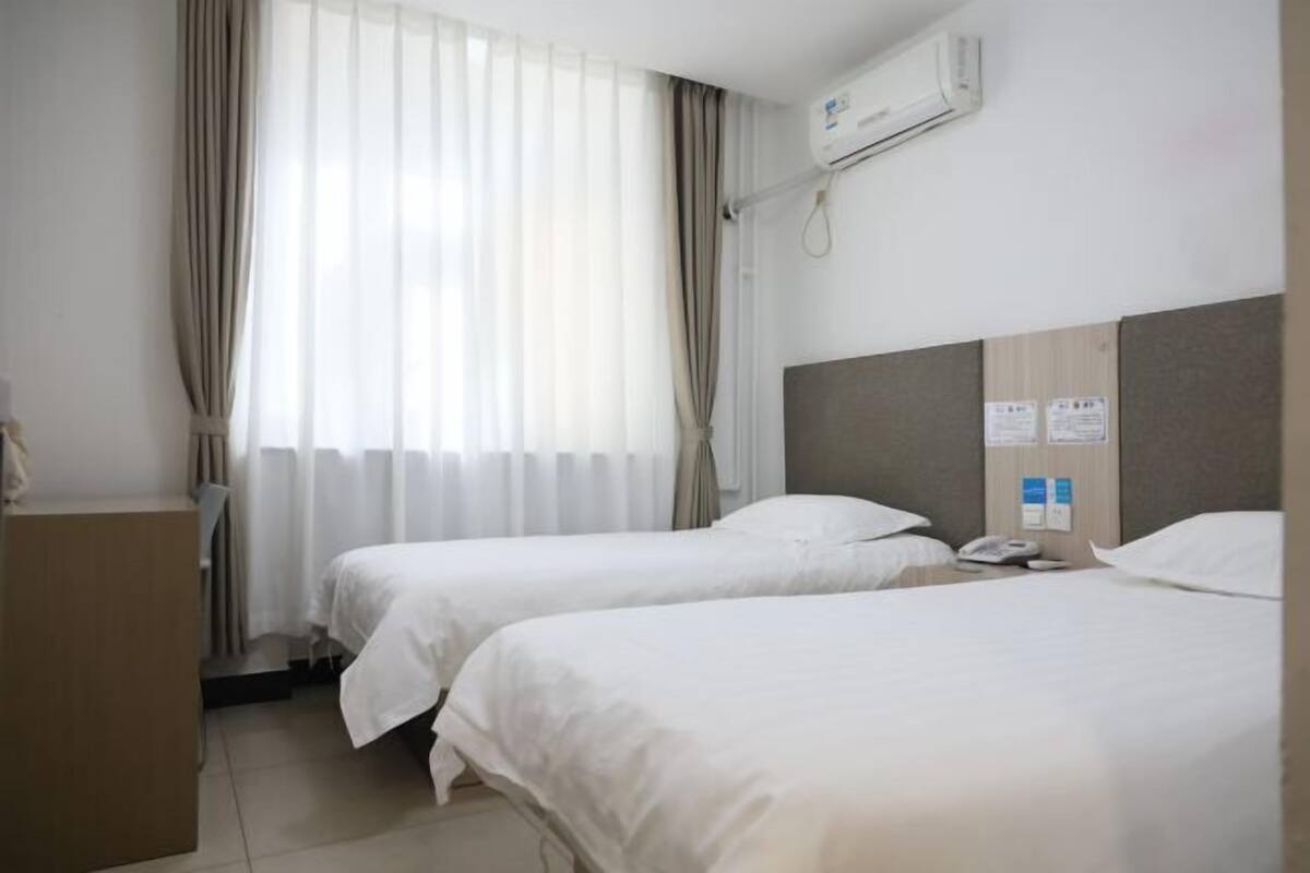 A hotel room with two beds, a desk, and an air conditioning unit.