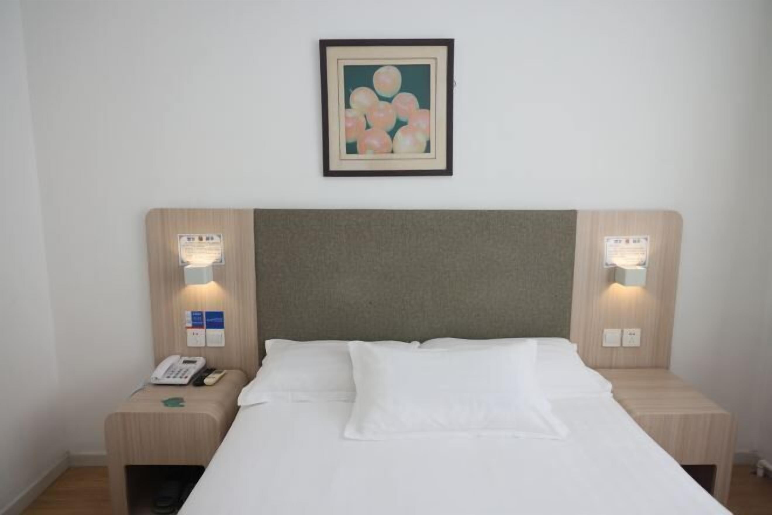Une chambre d’hôtel avec un lit, deux tables de chevet, un luminaire fixé au mur et un tableau encadré au-dessus du lit.