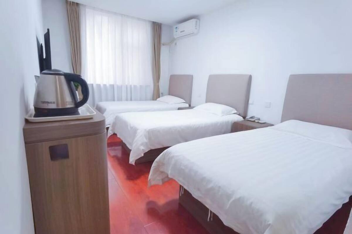 A hotel room with two single beds, a wooden cabinet, a kettle, and an air conditioning unit.