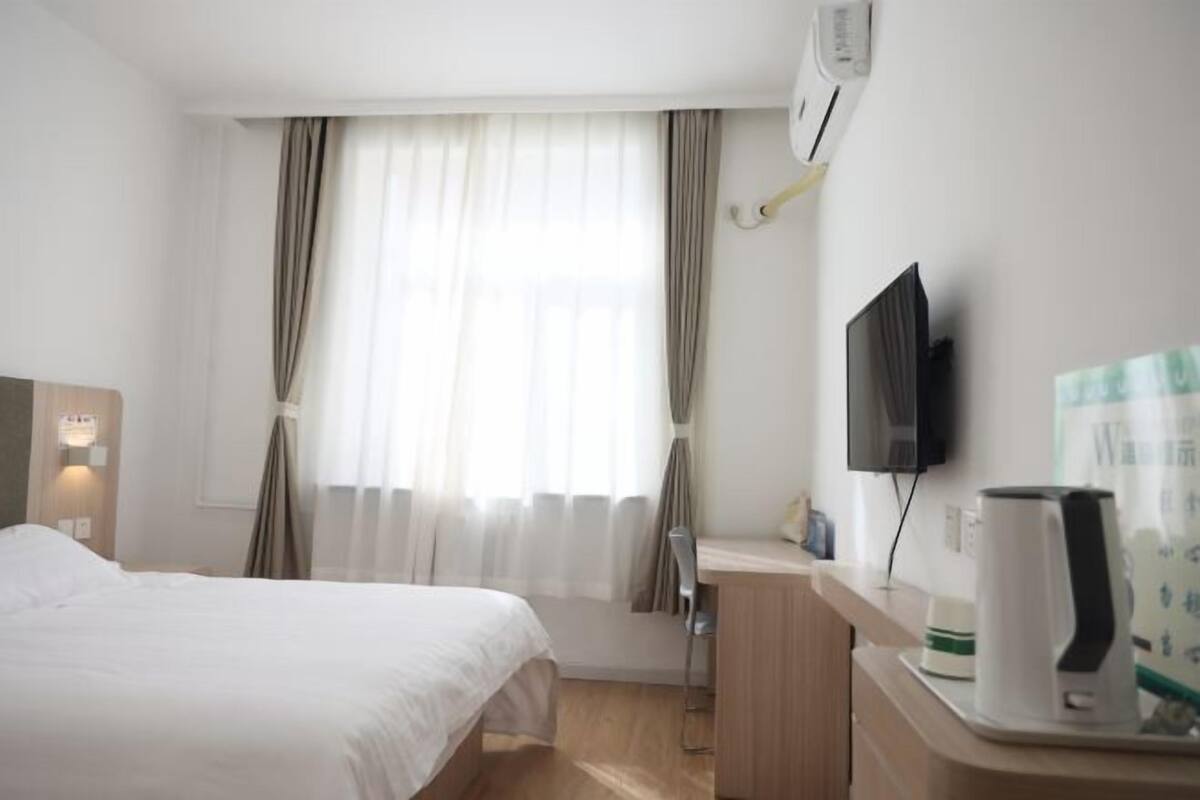 A hotel room with a bed, a desk with a kettle, a television, and curtains.
