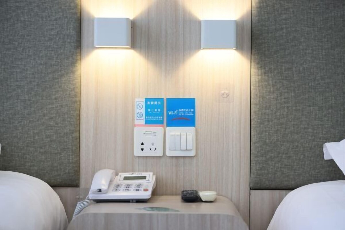 Et hotelværelse med en seng, en telefon på sengebordet, et kontrolpanel og et Wi-Fi-skilt.