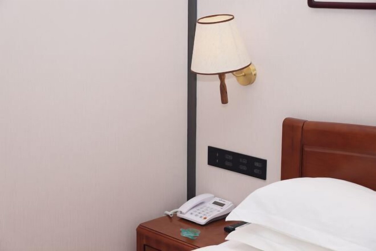 Et hotelværelse med sengegavl i træ, et natbord med telefon og lampe, samt et panel monteret på væggen.