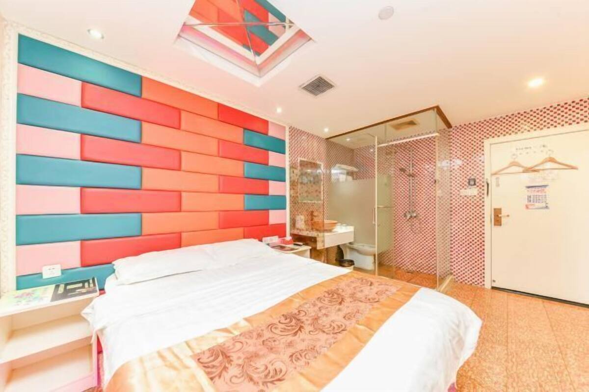 Une chambre d’hôtel avec un lit, un bureau, une douche et une porte sur laquelle est accroché un manteau.