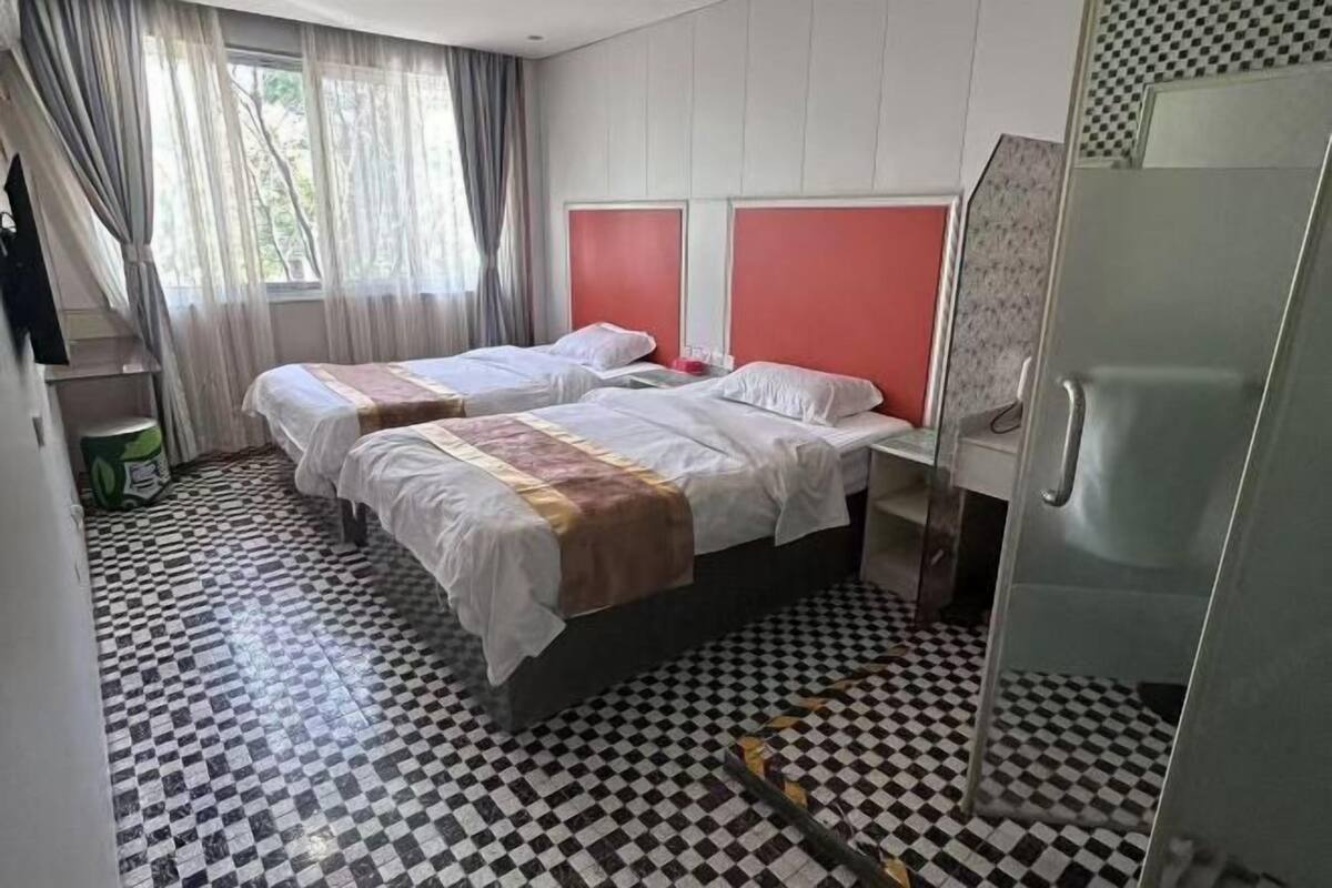 Une chambre d’hôtel avec deux lits, un sol à carreaux, un réfrigérateur et une fenêtre avec des rideaux.