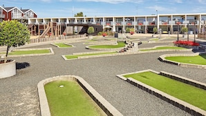 A courtyard with a children's play area, a small bridge, and a building with multiple balconies and outdoor seating. - 4 Person Holiday Home on Holiday Park in Glesborg (Glesborg)