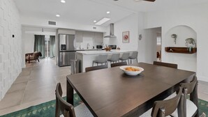 Une cuisine moderne dotée d’un îlot central, d’un coin repas avec une table et des chaises en bois, et d’un ventilateur de plafond.