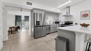 Une cuisine moderne dotée d’appareils électroménagers en acier inoxydable, d’un îlot central et d’un coin repas avec une chaise et des rideaux.