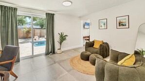 Un salon spacieux doté d’une grande porte-fenêtre coulissante donnant sur un jardin avec une piscine. On y trouve un coin salon confortable avec un canapé et un fauteuil.