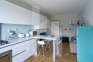 Une cuisine moderne avec des meubles blancs, un îlot central doté de tabourets, un four à micro-ondes, un grille-pain et un mixeur.