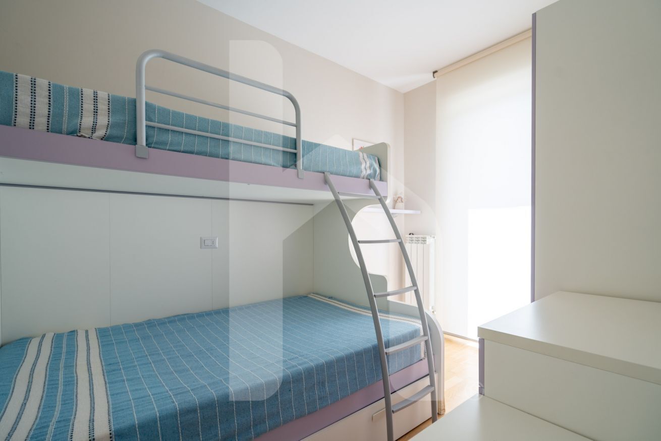 A bunk bed room with a ladder, a small white desk, and a window.