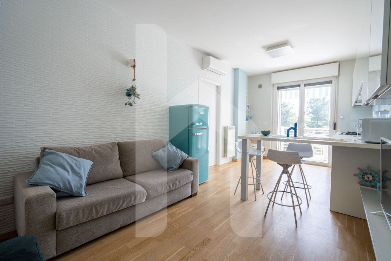 Un salon moderne avec un canapé, un coin cuisine équipé d’un réfrigérateur et une table à manger avec des chaises.