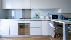 A modern kitchen with white cabinets, a built-in oven, a microwave, and a coffee maker. There are two bar stools and a small table with a bowl. - In an enchanting location, in a residential neighborhood a stone's throw from the city center and directly in the territory of the Marine Protected Area Torre del Cerrano, the I Gabbiani residence will offer you a relaxing holiday. The three-room apart (Foggetta)