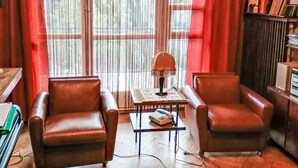 Un salon avec deux fauteuils en cuir, une petite table avec une lampe et une bibliothèque.