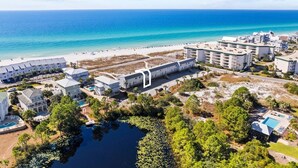 An aerial view of a coastal hotel with multiple buildings, a beach, and a small lake.