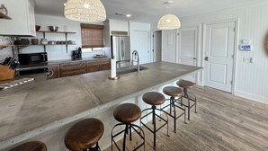 A modern kitchen with a large island, bar stools, pendant lights, and stainless steel appliances.