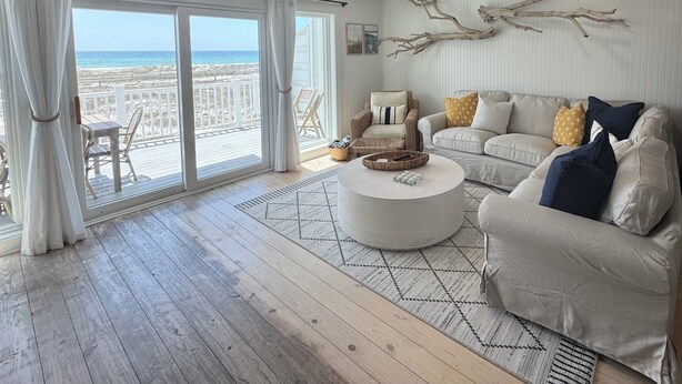 A spacious living room with a large sliding glass door leading to a balcony with a beach view.