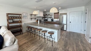 A modern kitchen with a central island, bar stools, pendant lighting, and a refrigerator.