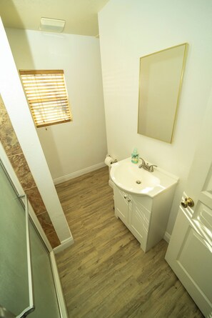 A bathroom with a white sink, a mirror, and wooden flooring.