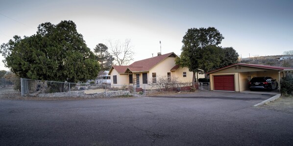 A single-story house with a red garage door, a fenced yard, and a parked car.