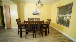 A dining area with a wooden table and chairs, a ceiling light fixture, a window with blinds, and a door.