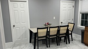 A dining area with a marble floor, a table with four chairs, and two white doors. - North End Relaxing Family (Manchester)