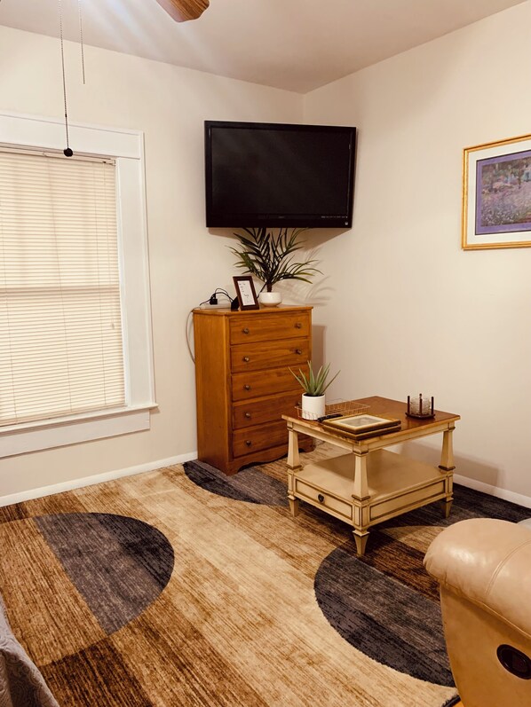 A living room with a wooden dresser, a small table, a television mounted on the wall, and a window with blinds. - The Studio on 8th, Entire guest suite in Wauchula Florida ! (Wauchula)