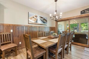 A dining area with wooden paneling, a chandelier, and a large window with a view of greenery. - Lakeview Home with Dock on the Whitefish Chain, Outdoor Pool, Pickleball & More (Pequot Lakes)
