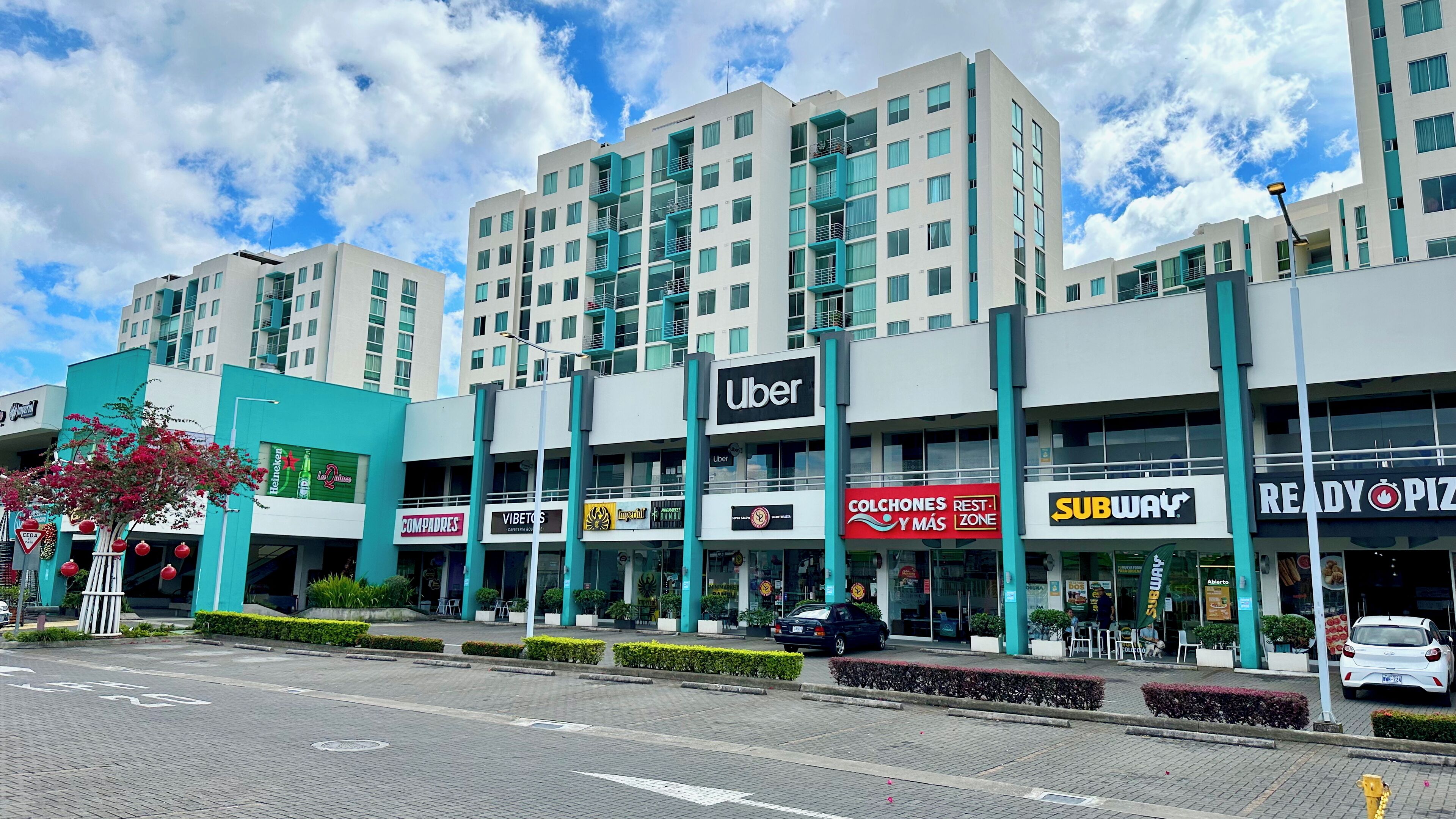 Un edificio moderno con varios locales comerciales, incluyendo un Subway y una pizzería Ready Pizza.