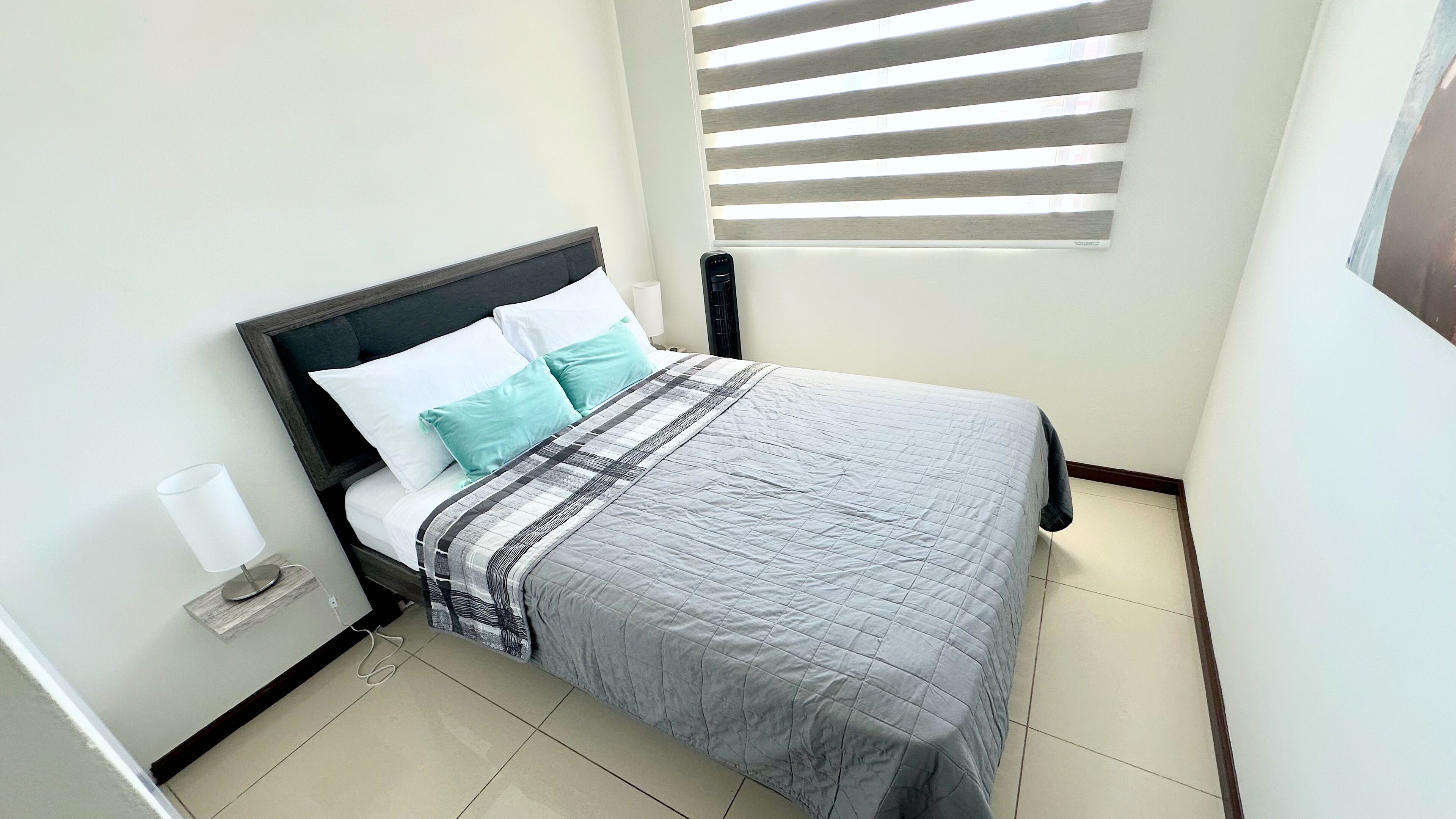 A neatly made bed with a grey quilt, white and teal pillows, and a dark headboard.