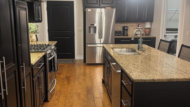 A modern kitchen with dark cabinetry, stainless steel appliances, a granite countertop, and pendant lighting.