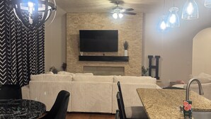 A modern kitchen with a central island, a dining area with a round table, and a living area with a sofa and TV.