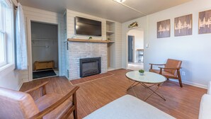 A living room with a fireplace, wooden flooring, a round coffee table, and a TV mounted on the wall. - Ely Basecamp- Perfect for Families and Groups (Ely)