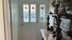 Un pasillo con piso de madera, alfombra estampada, puerta blanca con vidrieras y mueble de madera oscura con adornos.