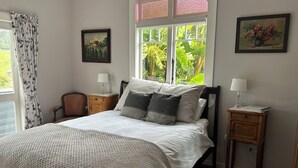 Un dormitorio ordenado con una cama grande, dos mesitas de noche, una ventana con vistas a zonas verdes y un cuadro en la pared.