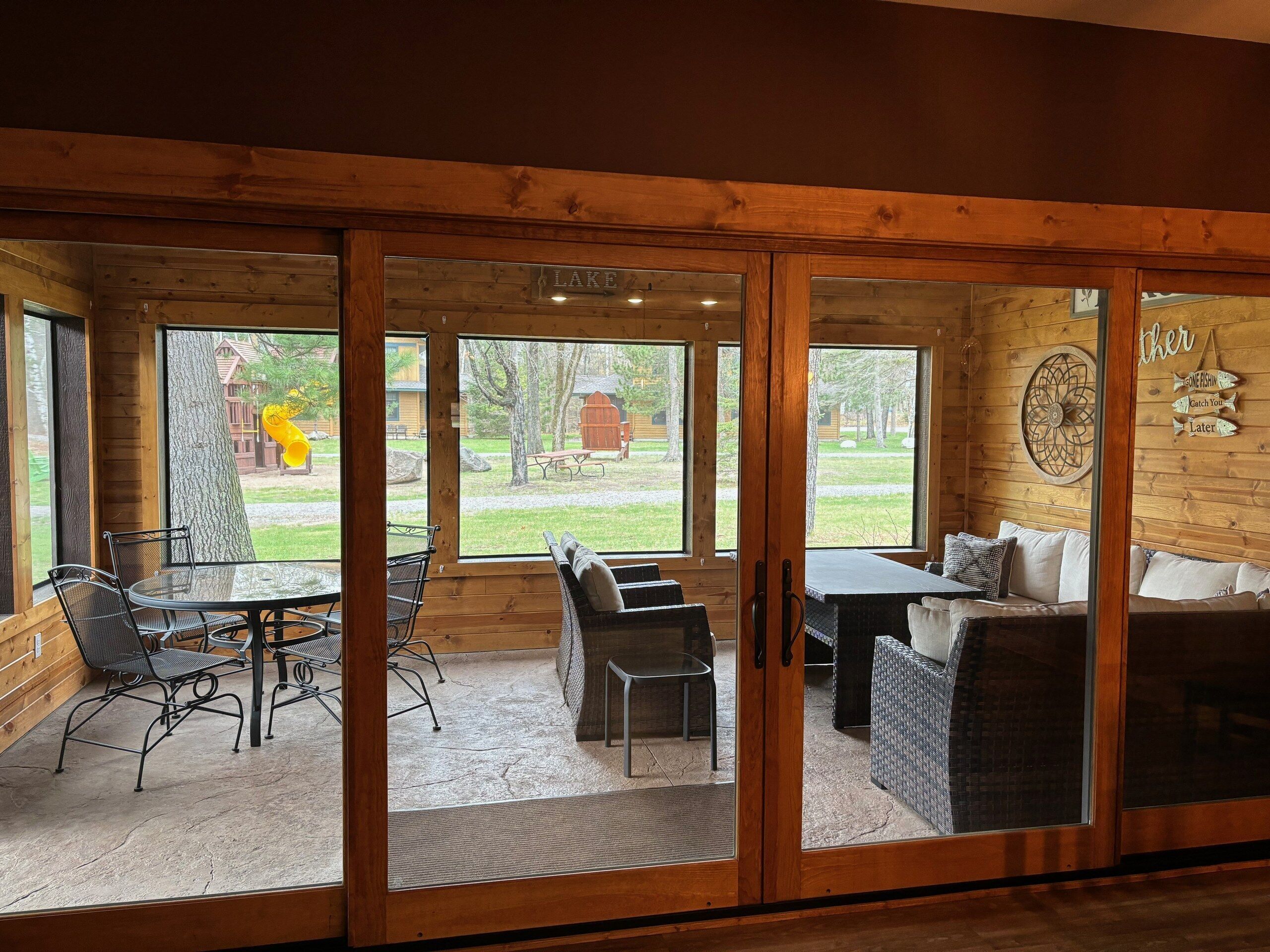 A wooden cabin with a dining area, a sofa, and a view of a yard with a wooden structure.