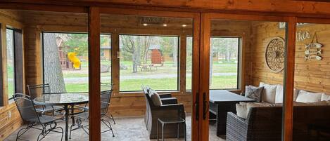 A wooden cabin with a dining area, a sofa, and a view of a yard with a wooden structure.