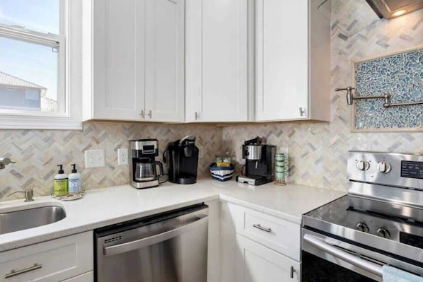 A kitchen with white cabinets, a dishwasher, a coffee maker, a toaster, and a stove.