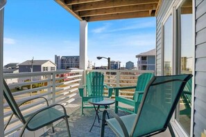 A balcony with green chairs and a table, overlooking a residential area with houses and a street.