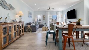 A spacious living area with a dining table, chairs, a sofa, and a television mounted on the wall.