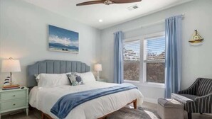 A bedroom with a bed, a nightstand, a chair, a window with curtains, and a ceiling fan.