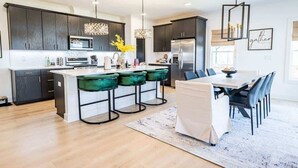 A modern kitchen with dark cabinets, a central island, bar stools, and a dining area with a table and chairs.