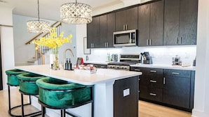 A modern kitchen with dark cabinets, a central island with bar stools, a microwave, and a sink. - Brand New-Downtown Apex-4BD/4BA-Gameroom-2 Kings! (Apex)