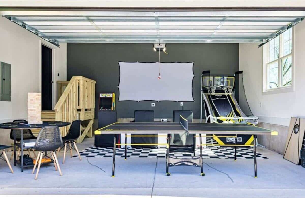 Un garage équipé d’une table de ping-pong, de chaises, d’un écran de projection et d’un panier de basket.