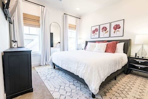 A bedroom with a bed, a nightstand, a dresser, a mirror, and framed artwork on the wall.